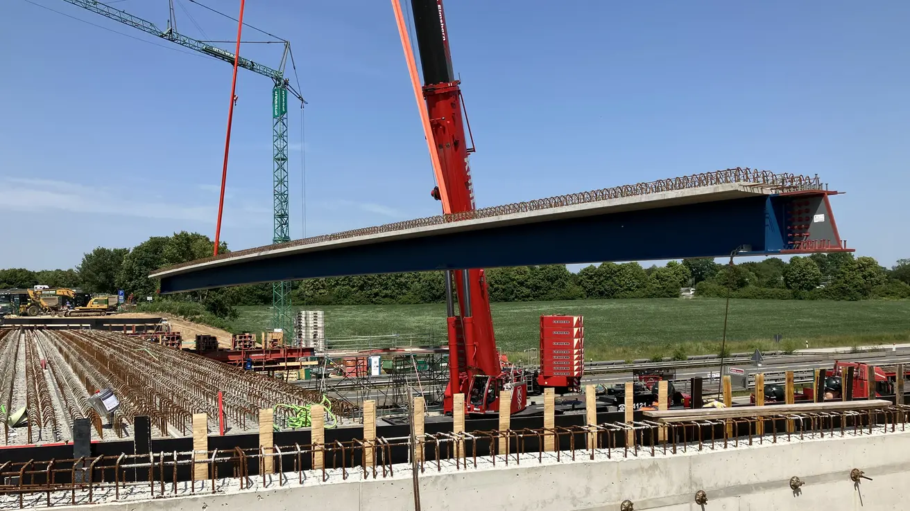 Während auf der einen Richtungsfahrbahn der Verkehr fließt, werden auf der anderen die Brückenträger bei bestem Wetter eingehoben.