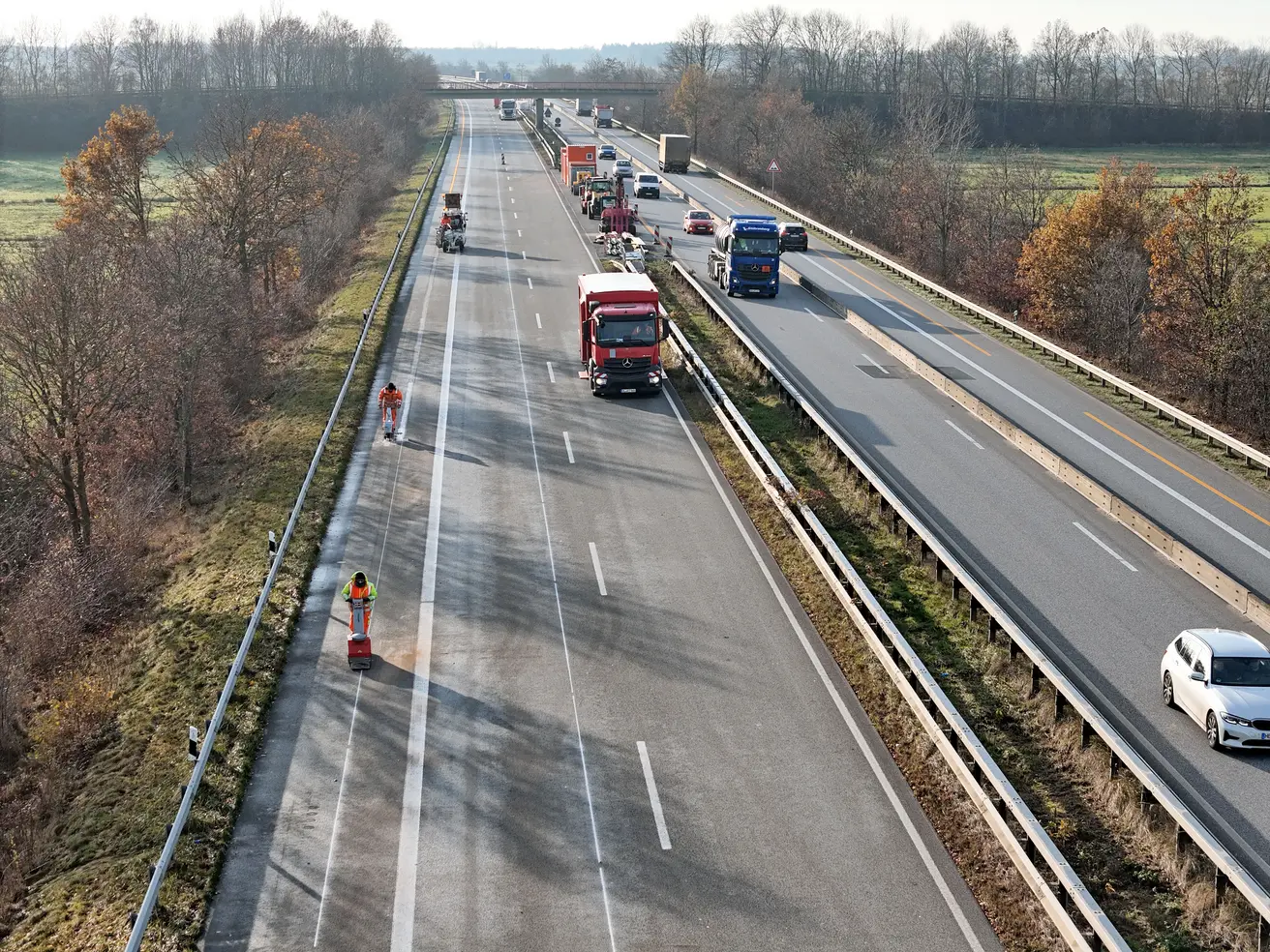 Fahrbahn trocknen (vorne), Kleber sprühen (Mitte) und Markierung von der Rolle aufbringen und andrücken (hinten) – die Markierungsarbeiten aus der Vogelperspektive. © Die Autobahn GmbH des Bundes