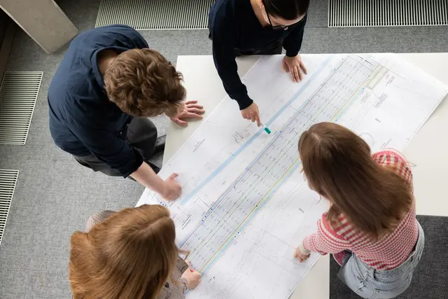 Mehrere Ingenieure sehen sich auf einem Tisch die Plannungen einer Brücke an. 