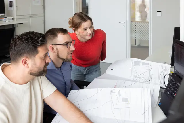 Zwei Bauingenieure zeigen einer Kollegin Ihr nächsten Brückenbauprojekt am Computer
