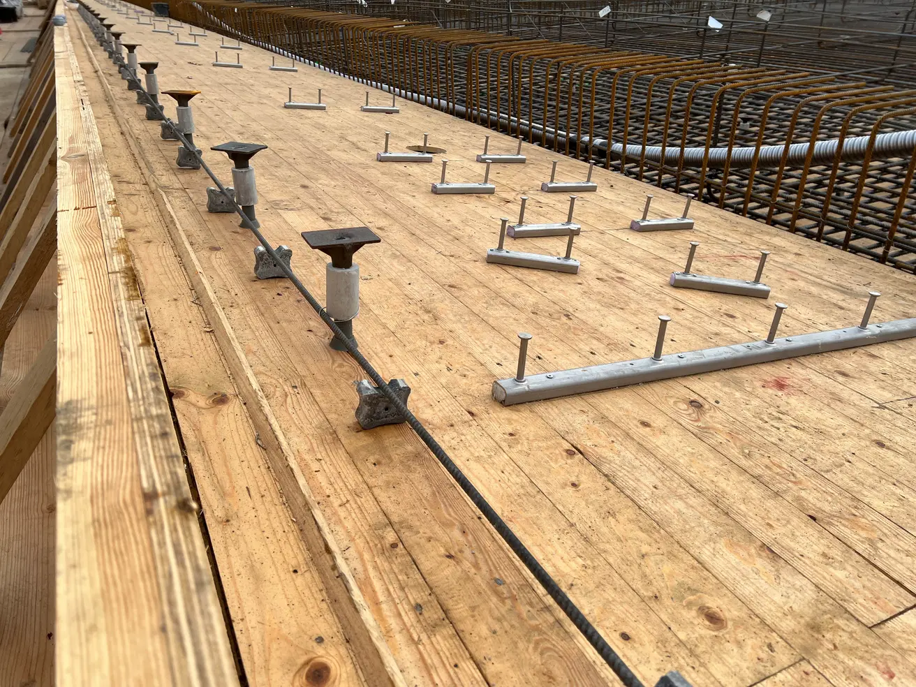 Die Verschalung für die westliche Brückenkappe. Ganz links: ein Bewehrungseisen (davon werden noch viel mehr verlegt). Links: sogenannte Koboldanker. An ihnen ist die Holzverschalung befestigt, damit sie nicht abfällt, wenn später das Traggerüst demo Die Verschalung für die westliche Brückenkappe. Ganz links: ein Bewehrungseisen (davon werden noch viel mehr verlegt). Links: sogenannte Koboldanker. An ihnen ist die Holzverschalung befestigt, damit sie nicht abfällt, wenn später das Traggerüst demontiert wird. Rechts: Ankerschienen. Sie werden ebenso wie die Koboldanker einbetoniert. Später werden daran von unten die Entwässerungsleitungen befestigt. © Die Autobahn GmbH des Bundes