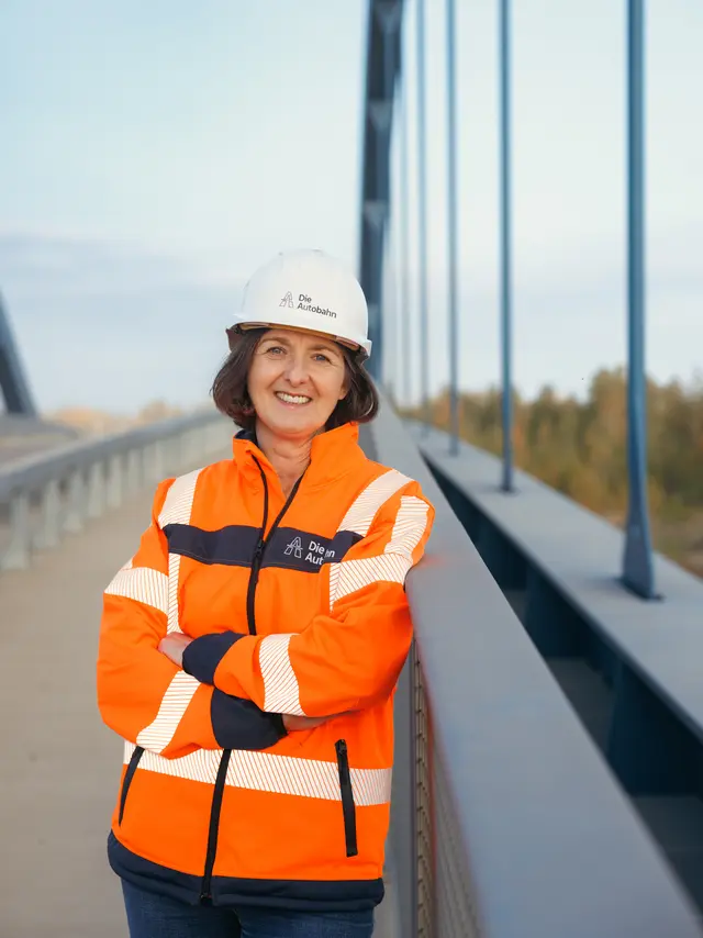 Eine Bauingenieurin steht lächelnd mit verschränkten Armen auf einer fertigen Brücke.