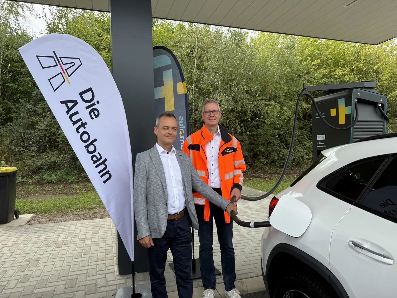 Der Schnellladepark Kutzhof-Süd ist eingeweiht: Dr. Burkhard Seizer, Geschäftsführer autostrom plus GbmH und Markus Gerhards, Direktor der Niederlassung West der Autobahn GmbH des Bundes, laden vor Ort das erste Fahrzeug.