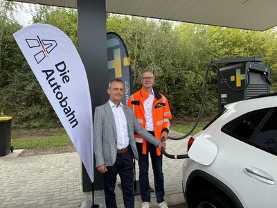 Der Schnellladepark Kutzhof-Süd ist eingeweiht: Dr. Burkhard Seizer, Geschäftsführer autostrom plus GbmH und Markus Gerhards, Direktor der Niederlassung West der Autobahn GmbH des Bundes, laden vor Ort das erste Fahrzeug.