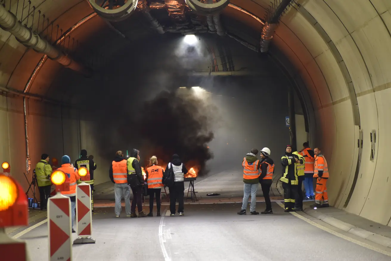Blick in die erleuchete Tunnelröhre. Im Hintergrund das qualmende Feuer und Menschen.